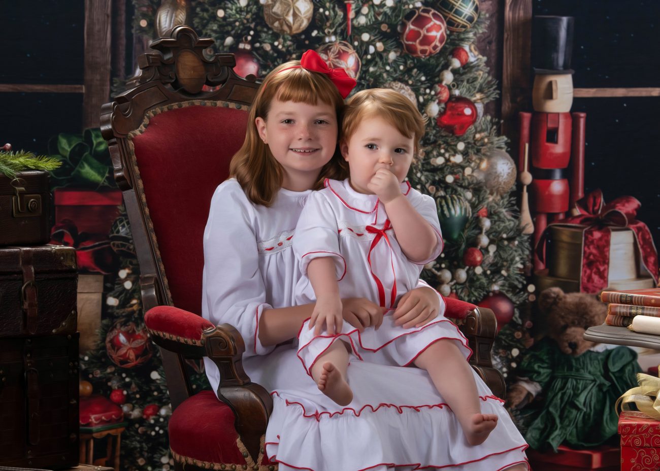 Two sisters in white nightgowns on a red velvet chair by the tree, a Blackwater fine art Christmas portrait