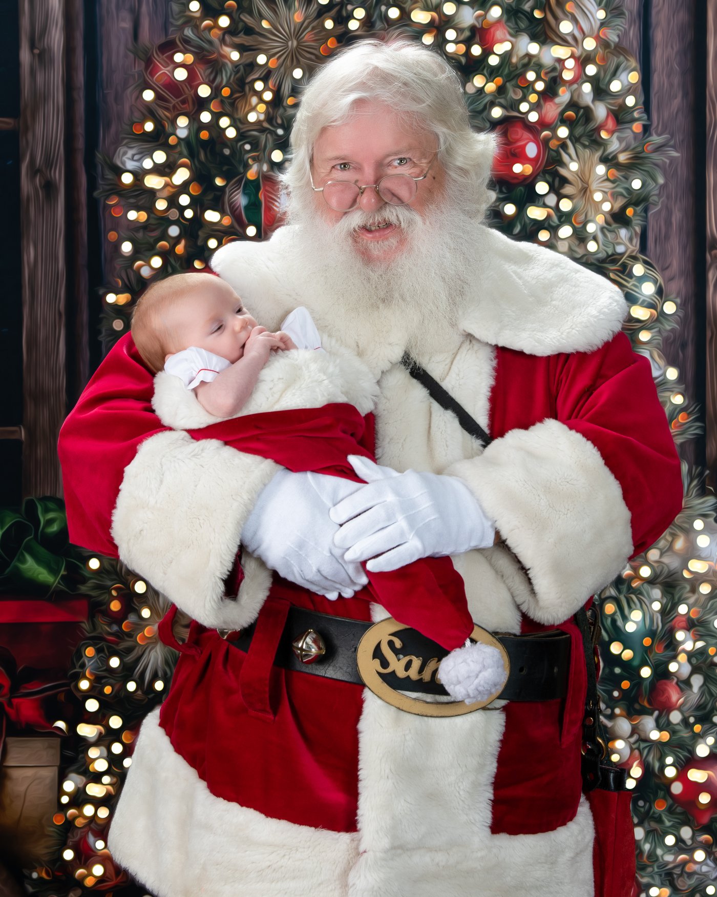 Santa cradling a newborn in front of a lit Christmas tree, a Blackwater fine art Santa portrait
